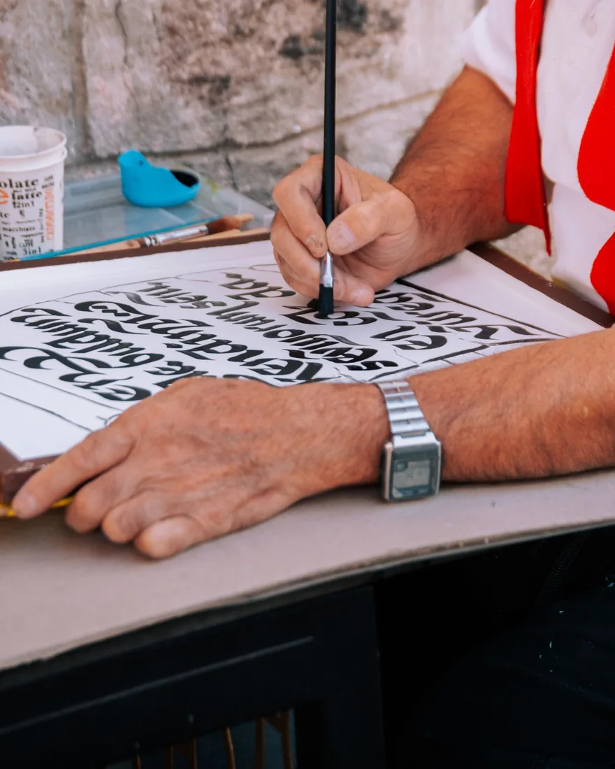 Manos apoyadas sobre una tabla mientras un pincel perfila letras negras trazadas a mano